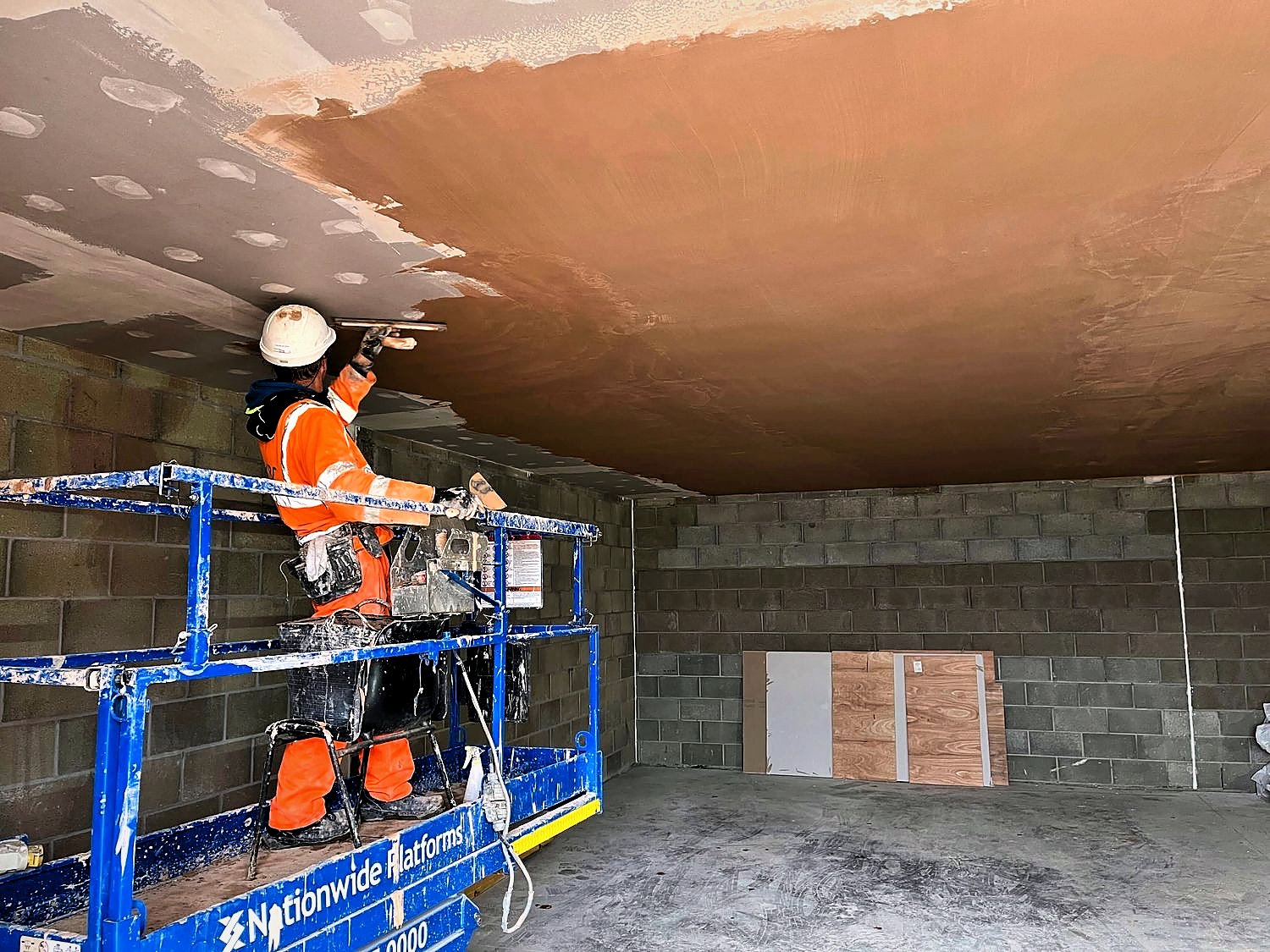 PKBC operative finishing a ceiling from a powered access platform inside a blockwork industrial building