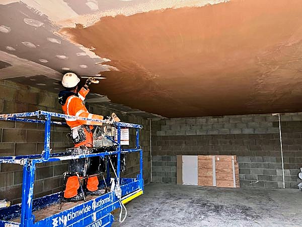 Operative finishing a ceiling from a powered access platform inside a blockwork building