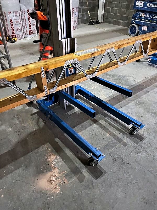 Material lift supporting a metal web timber joist during installation inside an industrial unit