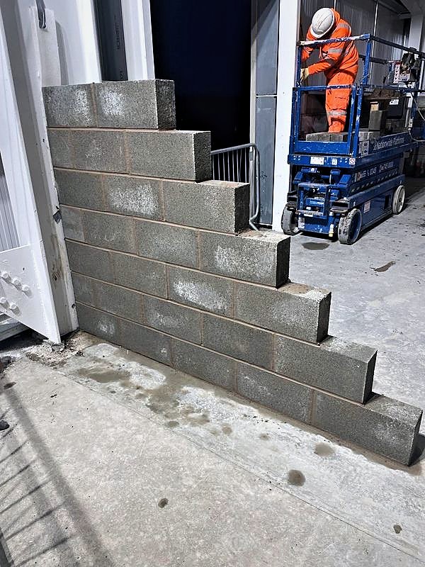 Racked blockwork wall stepped back beside a door opening, scissor lift behind