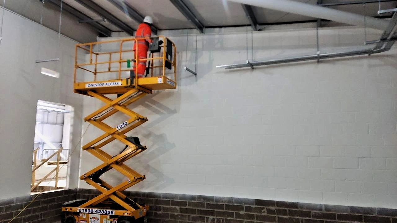 Operative working from a scissor lift at high level inside a painted blockwork substation building