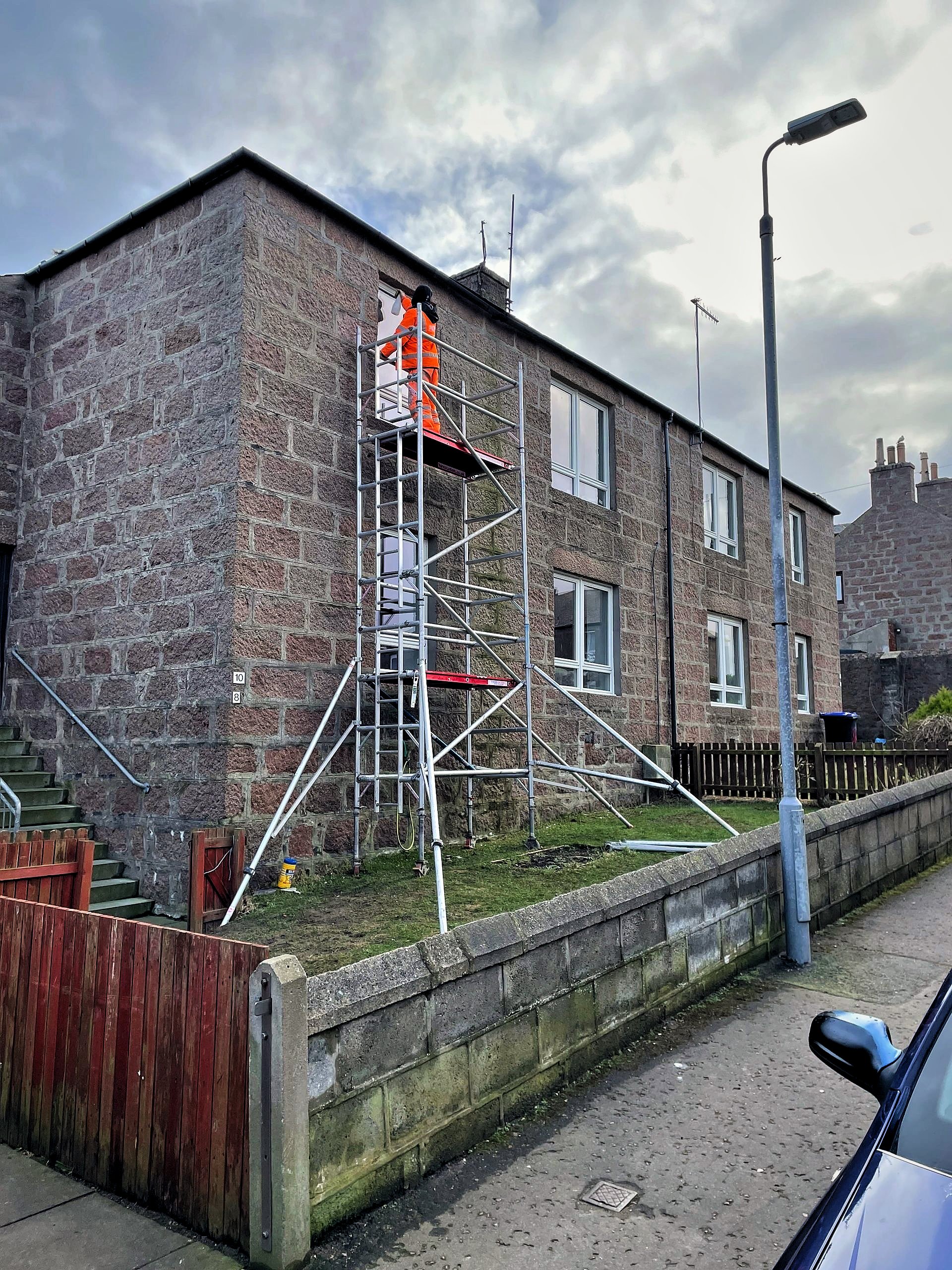 Operative replacing an upstairs window from a scaffold tower on a granite terraced house