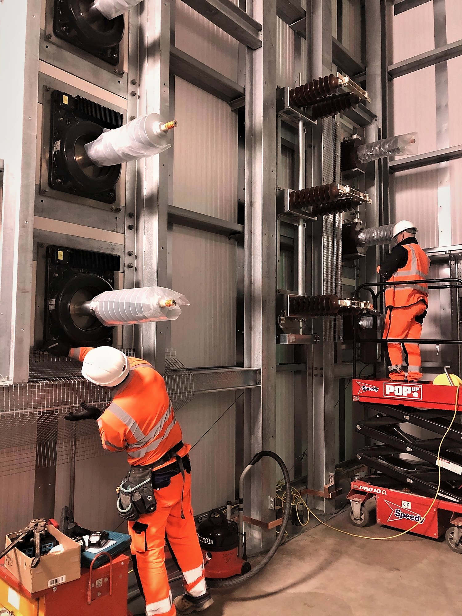 Operatives on access platforms installing HV switchgear and bushings inside a substation building