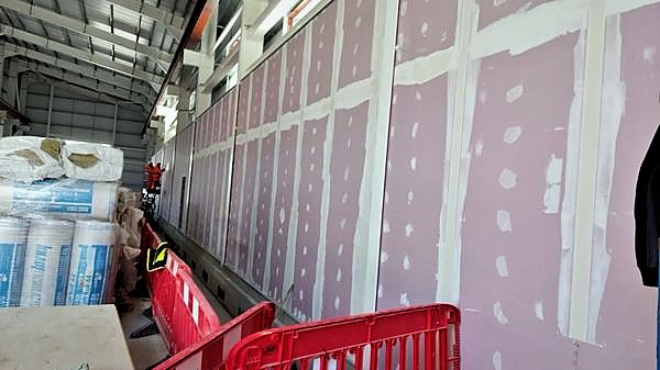 Long run of taped and jointed partition wall behind safety barriers