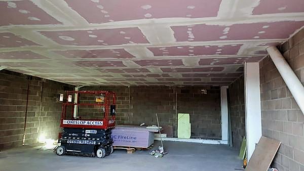 Taped and jointed plasterboard ceiling over blockwork walls with a scissor lift below