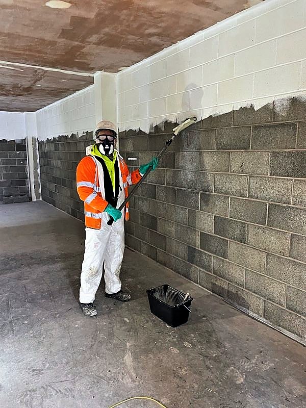 Operative in a respirator applying the first coat to blockwork with a roller