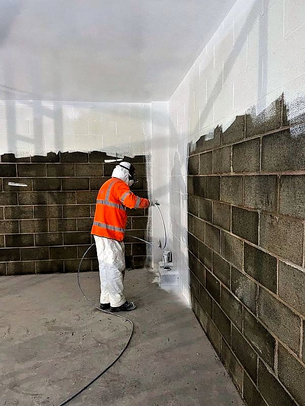 Operative spray painting a blockwork wall white
