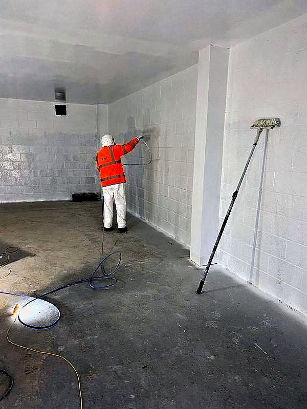 Operative spray painting a blockwork room white