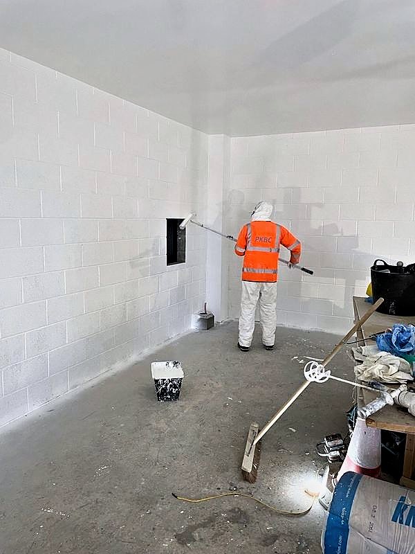 PKBC operative roller painting a blockwork wall white