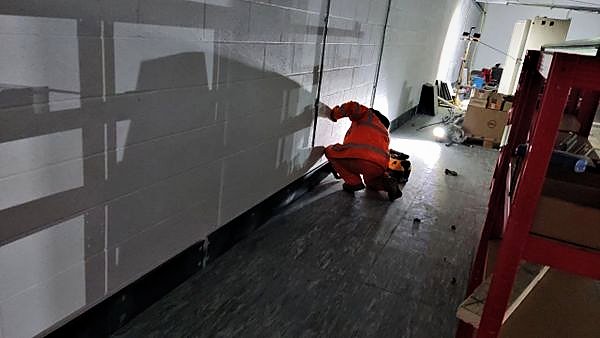 Operative working at the base of a painted blockwork wall beside a protected floor