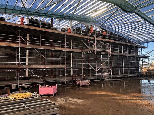 Multi-lift scaffold along a large blockwork facade with operatives at several levels