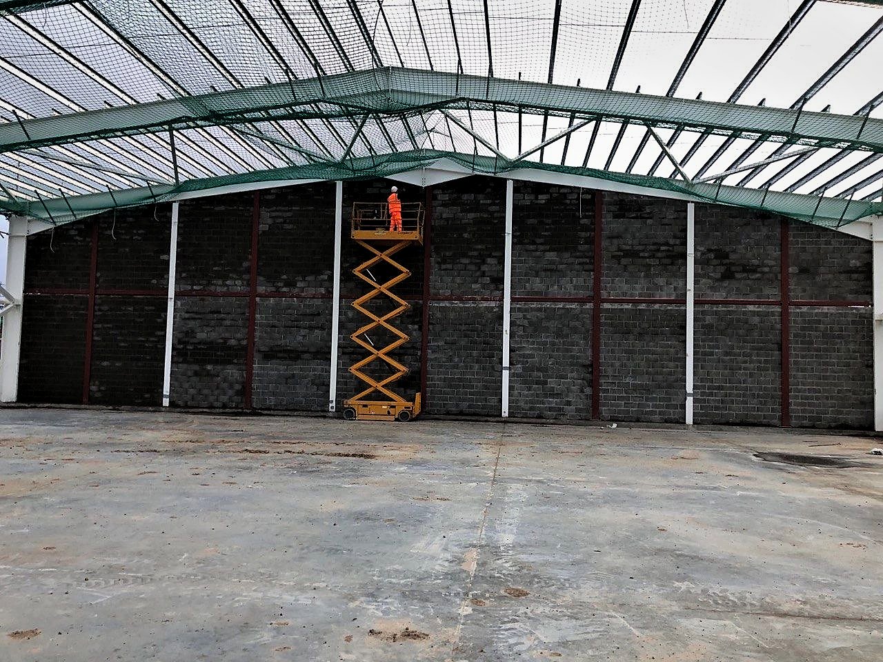 Operative on a scissor lift building a full-height blockwork gable inside a steel-framed building