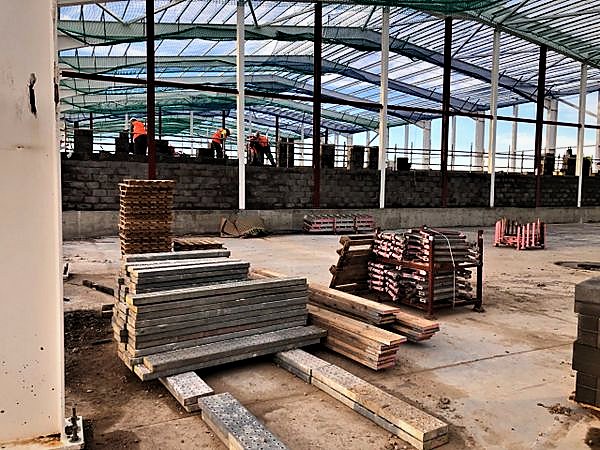 Bricklayers building a perimeter blockwork wall inside a netted steel frame
