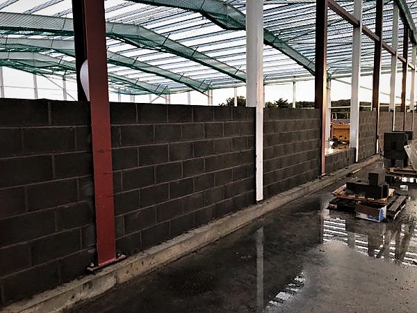 Long run of dense blockwork between steel columns under a netted roof