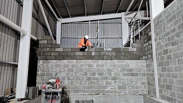 Bricklayer topping out a stepped blockwork wall from a tower scaffold