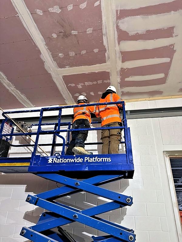 Operatives on a scissor lift jointing a plasterboard ceiling above a blockwork wall