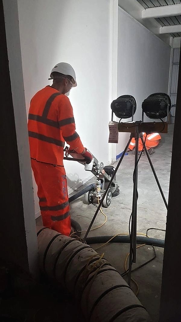 Operative grinding a floor slab under tripod lighting