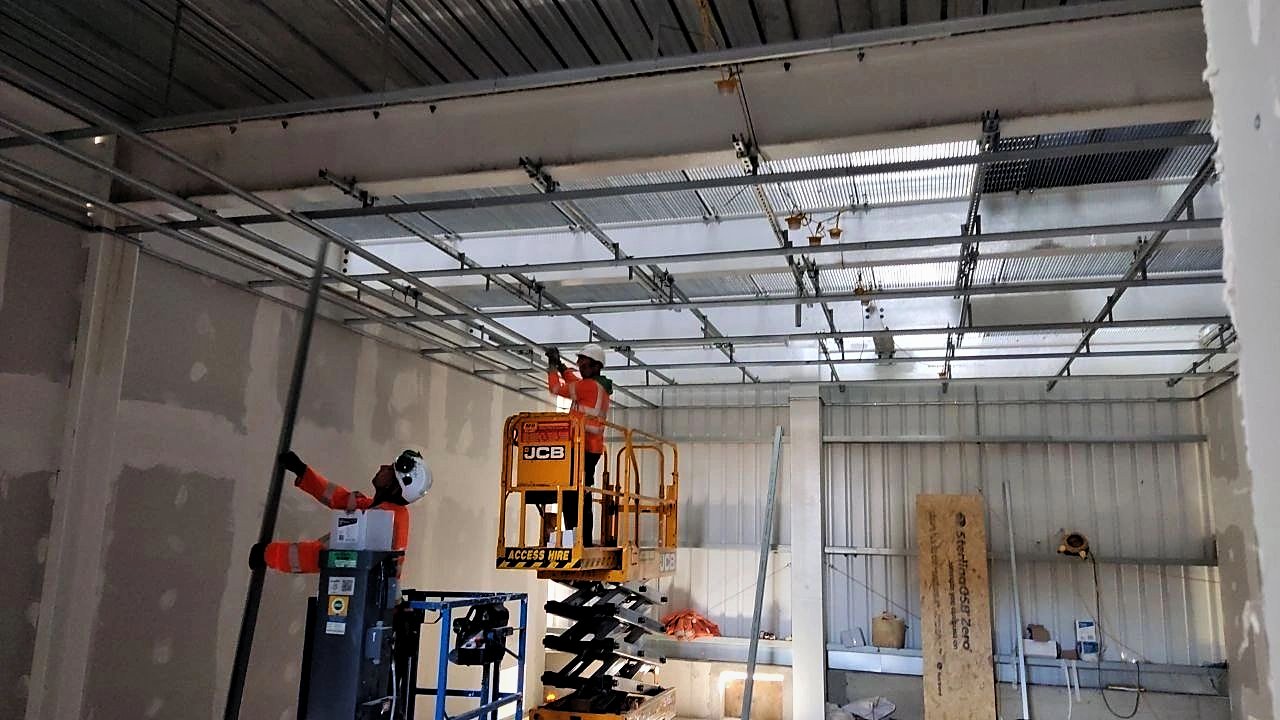 PKBC operatives installing a suspended ceiling grid from powered access inside a steel-framed building