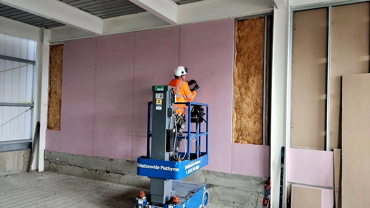 PKBC operative boarding a full-height stud wall from a powered access platform