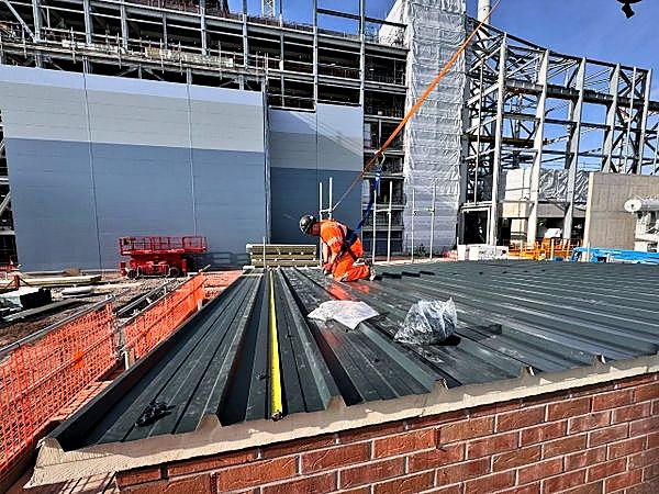 Operative in a harness fixing insulated roof panels on a plant room roof