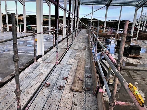 Boarded scaffold walkway with double guardrails along a steel portal frame