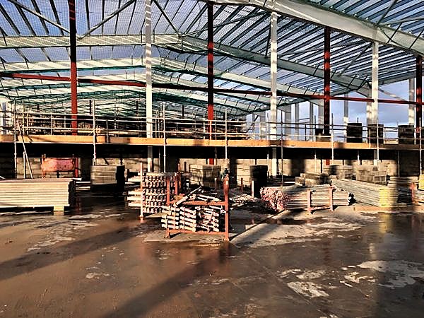 Scaffold access platform along first-lift blockwork inside a steel-framed hall