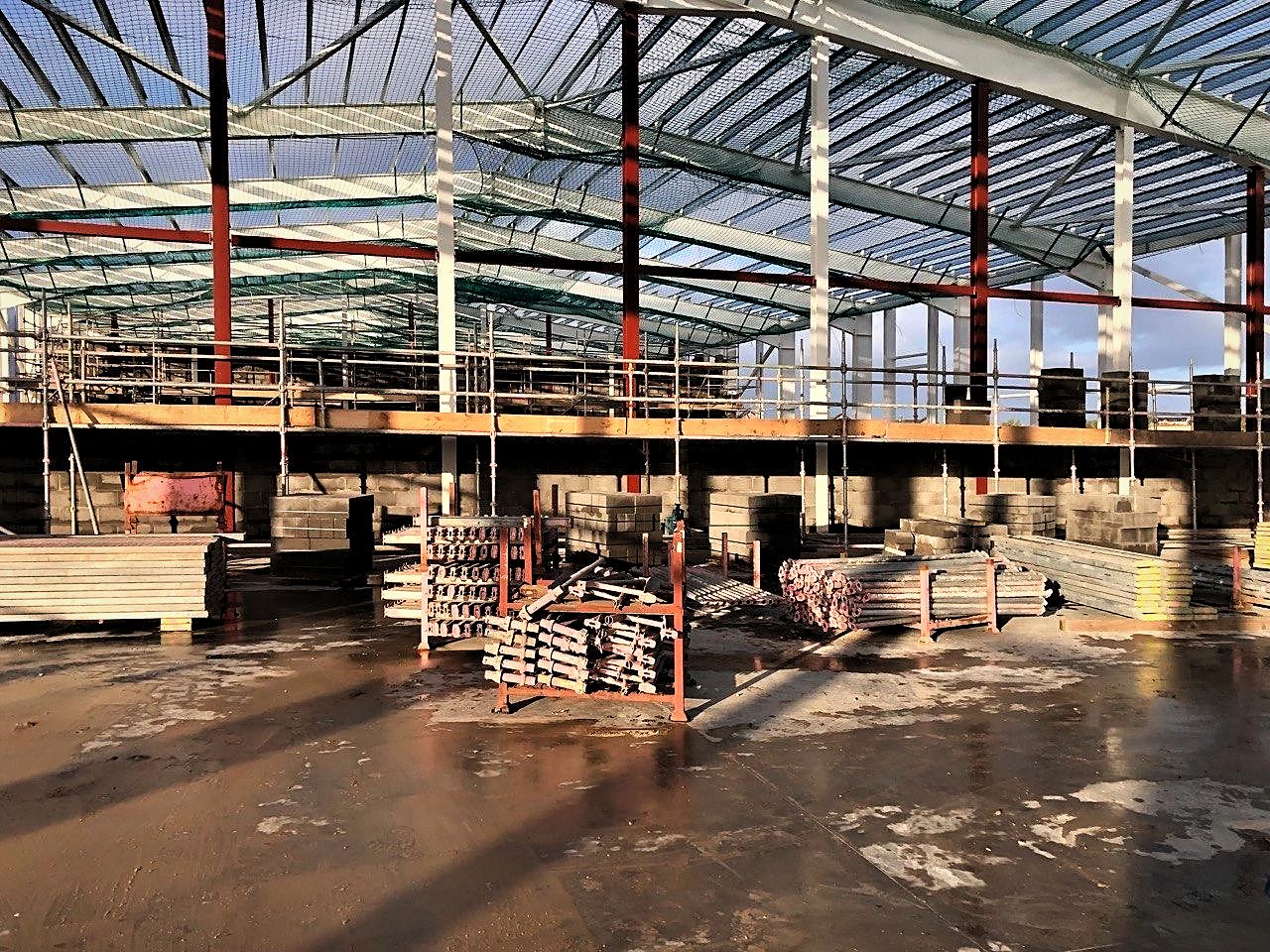 Scaffold access platform with guardrails along first-lift blockwork inside a steel-framed industrial building