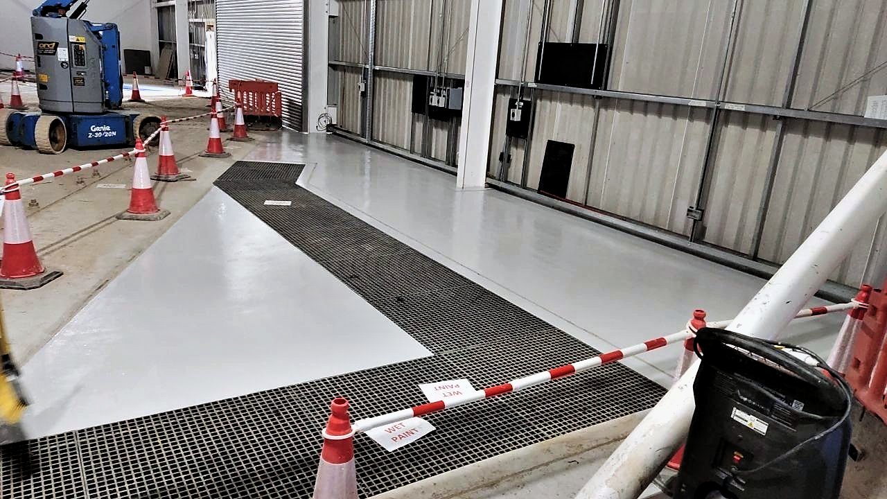 Freshly coated industrial floor marked with wet paint signs and cones inside a steel-clad building