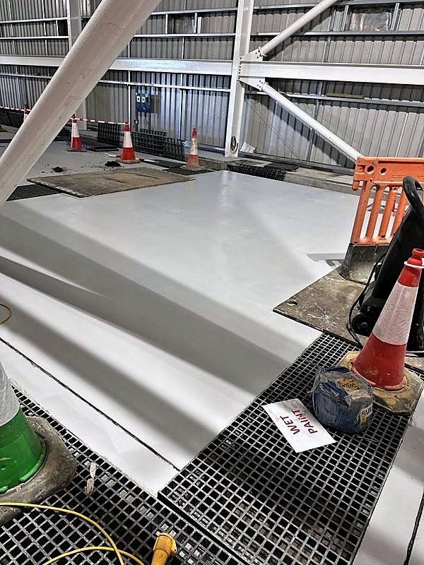 Freshly coated equipment plinth beside GRP grating walkways inside a plant building