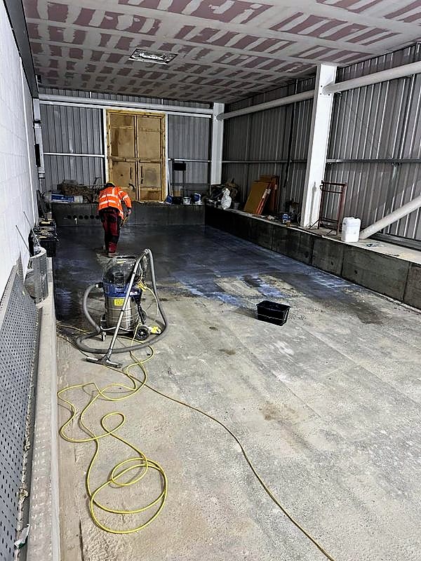Operative preparing a concrete floor inside a steel-framed industrial building