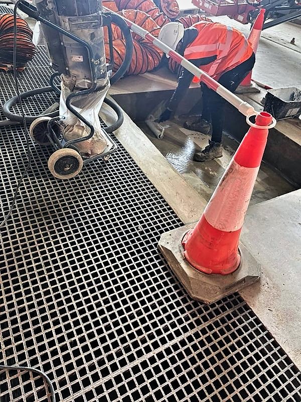 Dust-controlled preparation works in a coned-off area beside open floor grating