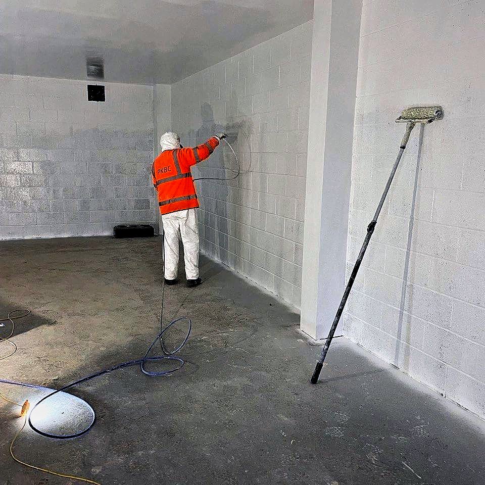 Operative spray painting blockwork walls white inside a substation building