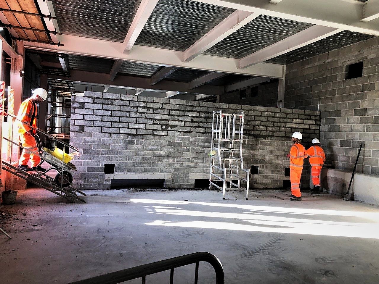 Operatives building blockwork walls inside a steel-framed substation building